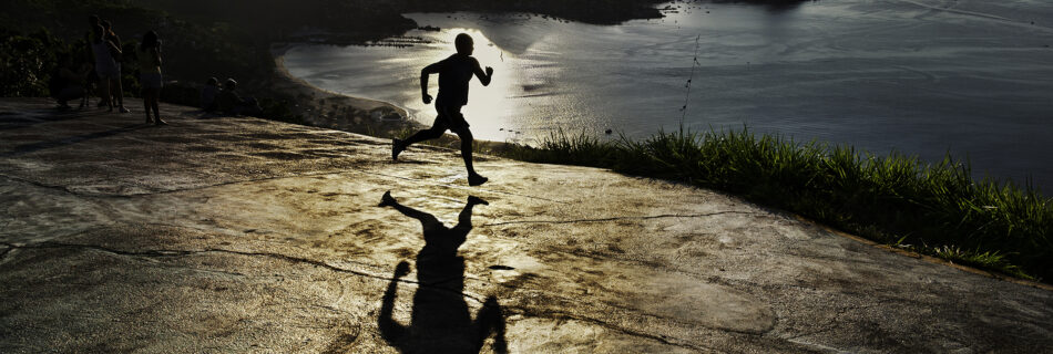 In Steve McCurry's 2009 photograph of a man running at dawn in Rio de Janeiro, Brazil, the early morning atmosphere is captured with McCurry’s trademark sense of color and composition. The runner, silhouetted against the warm, golden hues of the sunrise, moves along a coastline that is both vast and serene, with Rio’s iconic mountains rising majestically in the background. The image conveys a powerful sense of solitude and focus, as the lone figure embraces the peaceful quiet of dawn in one of the world’s most vibrant cities. McCurry’s eye for detail highlights not only the natural beauty of the scene but also the universal human drive for perseverance and inner strength. This image, like many of McCurry’s works, merges the beauty of the landscape with a moment of human resilience, creating a scene that feels both intimate and expansive.